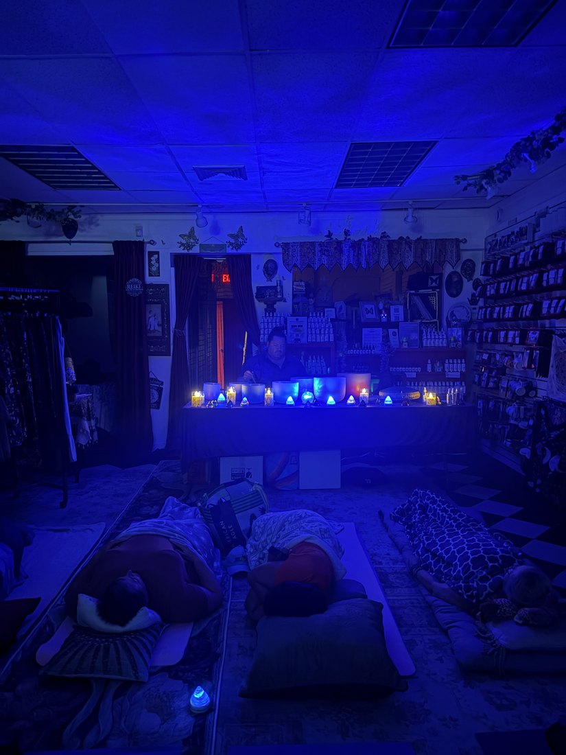 The room during the Pisces full moon sound bath, lit deep blue, with guests resting on mats and blankets while the crystal singing bowls are played at the front